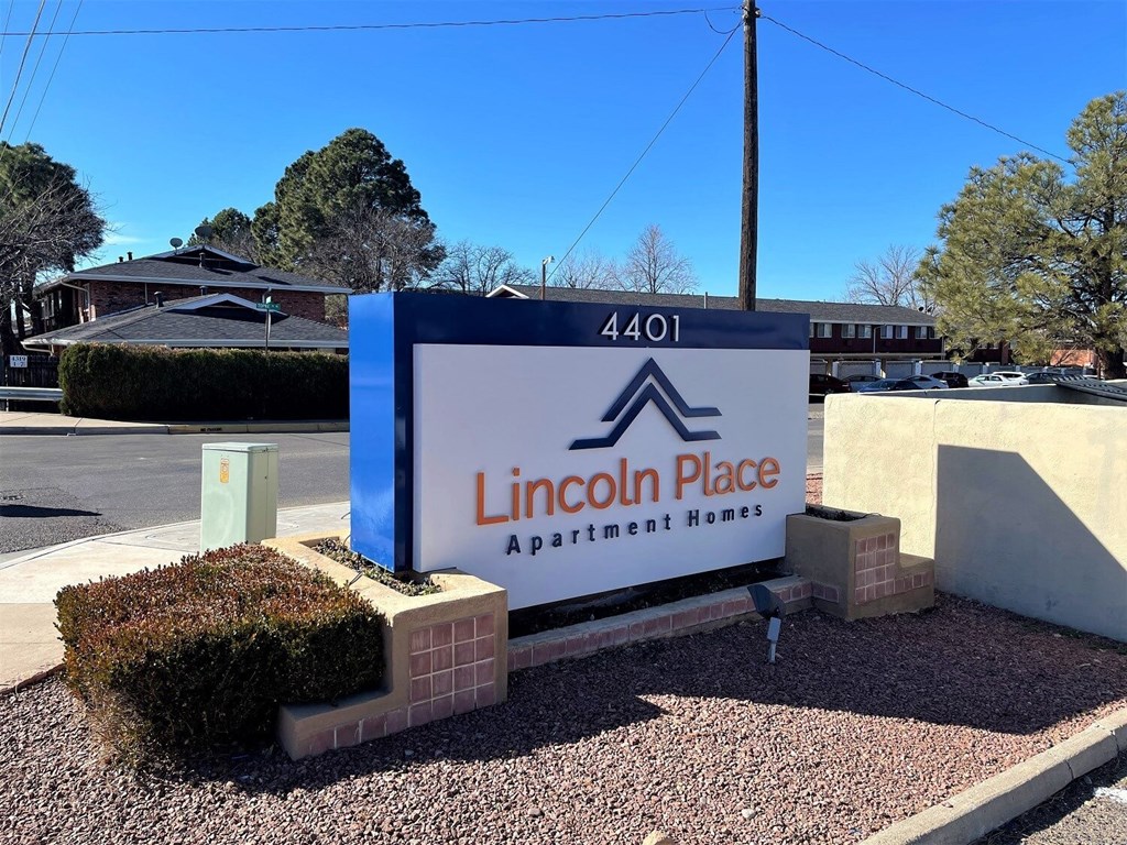 A blue and white sign for Lincoln Place Apartment Homes sits in front of a building.